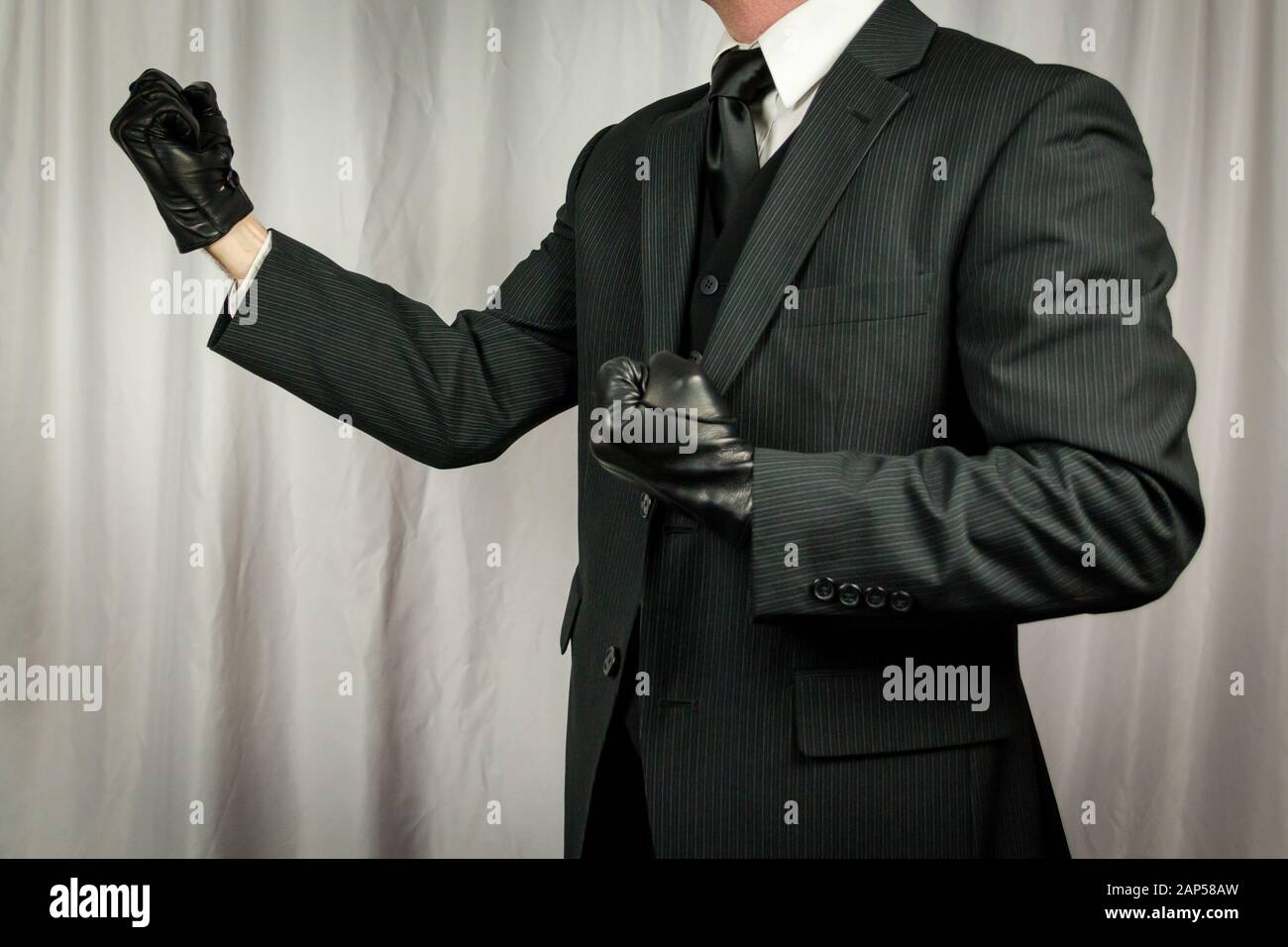 Man in Dark Suit and Leather Gloves in Fighting Stance. Concept of Classic and Eccentric British Gentleman. Retro Fashion. Stock Photo