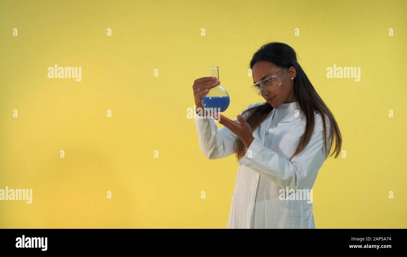 Black female scientist in lab coat looking on flask with experimental ...