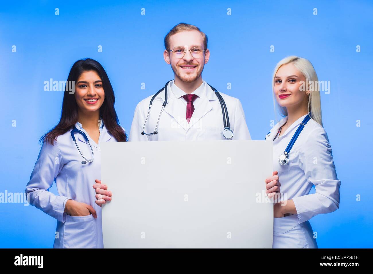 A team of young doctors with a sheet of white paper in his hands.. Multinational people - doctor, nurse and surgeon in blue background. A group of med Stock Photo