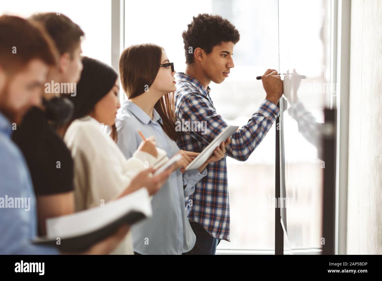 Students writing algebra equations on whiteboard in classroom Stock Photo