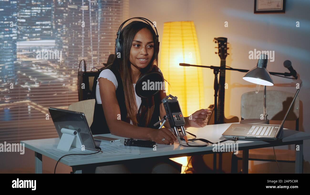 Multiracial female journalist doing online interview on the computer in  home recording studio in the evening. Woman is in headphone Stock Photo -  Alamy