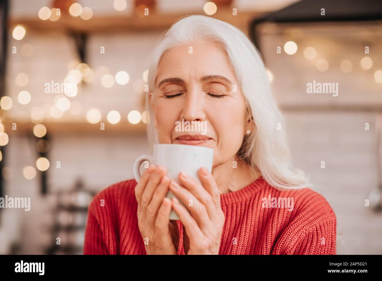 Beautiful elderly woman in red blouse smelling her tea Stock Photo