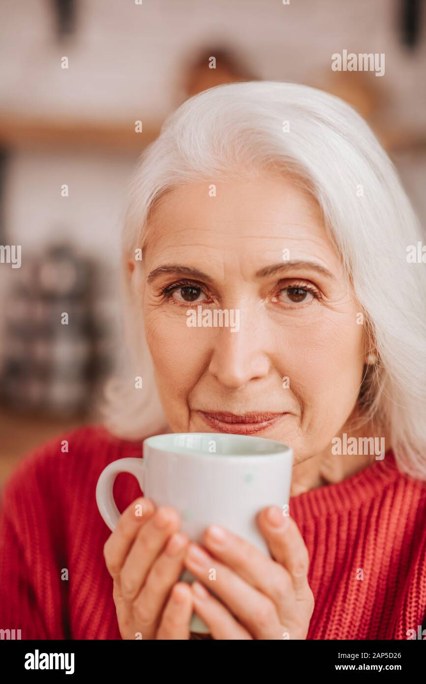 Beautiful elderly woman in red blouse enjoying her tea Stock Photo