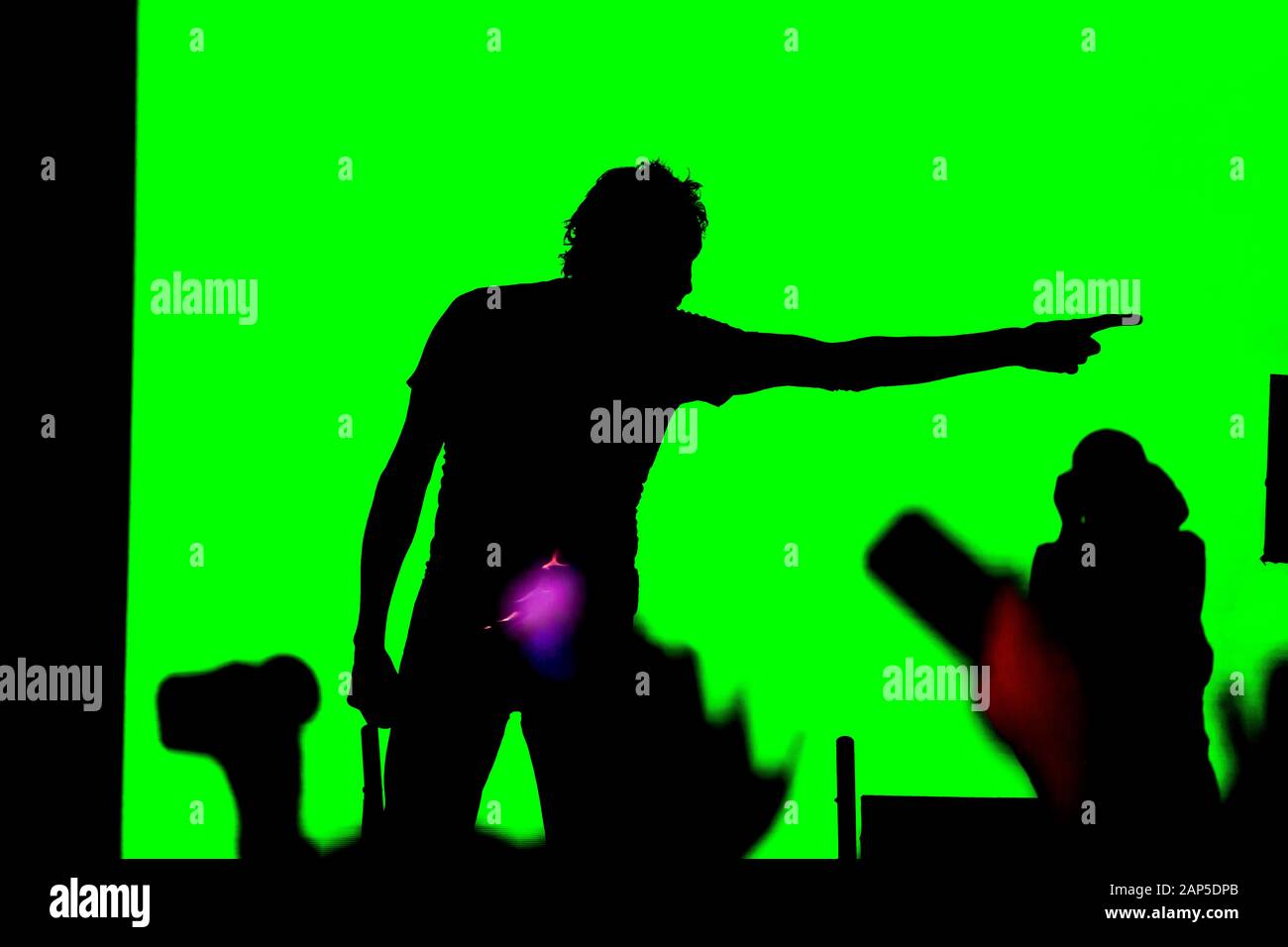 Male rock musician sings on stage into a microphone. silhouette on a green background Stock Photo