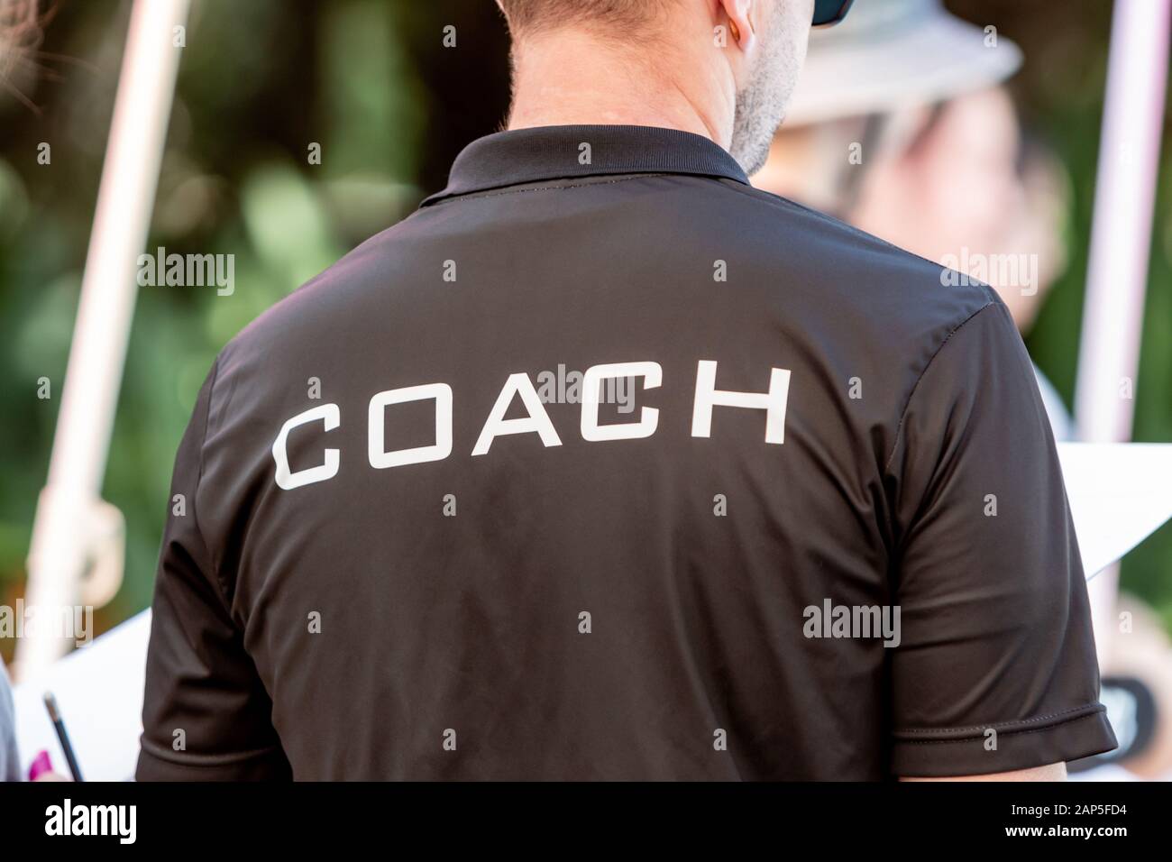 Back view of a male coach wearing black coach shirt with the white word