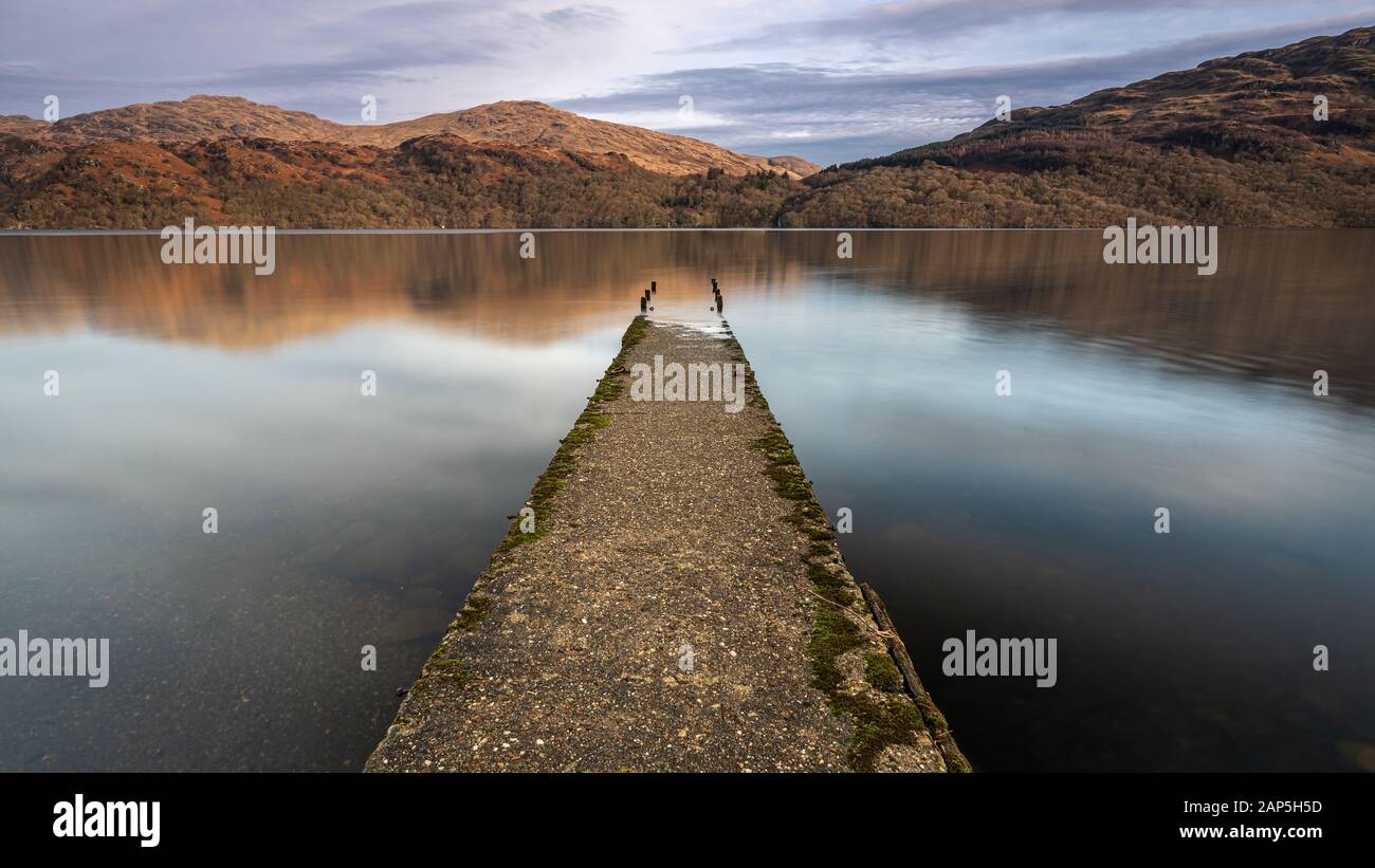 A long exposure of an old jetty on the shore of Loch Lomond, Scotland.  Looking over to Inversnaid and the mountains of Loch Lomond National Park. Stock Photo