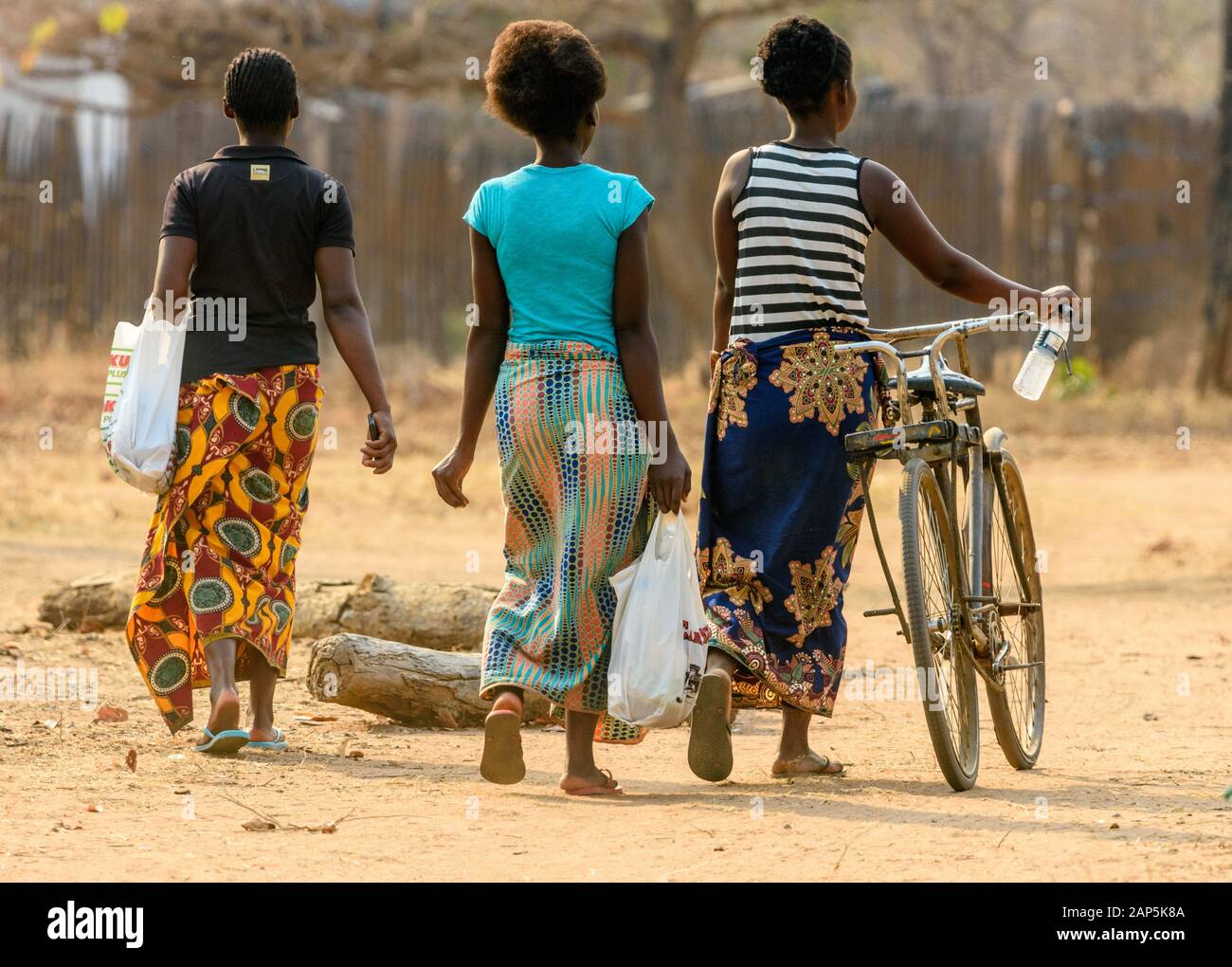 three. young Malawian women walking and pushing a bicycle along a dirt road in a township Stock Photo