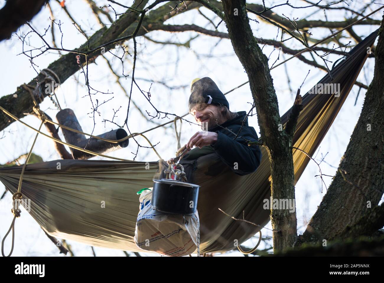 Harefield, UK. 21 January, 2020. An activist lying in a hammock suspended high up in a tree at the Save the Colne Valley wildlife protection camp enjoys a pot of breakfast porridge. Activists seeking to protect ancient woodland threatened by the HS2 high-speed rail link continue to occupy both the roadside and woodland sites of the camp having retaken it from bailiffs acting on behalf of HS2 on 18th January. 108 ancient woodlands are set to be destroyed by HS2. Credit: Mark Kerrison/Alamy Live News Stock Photo