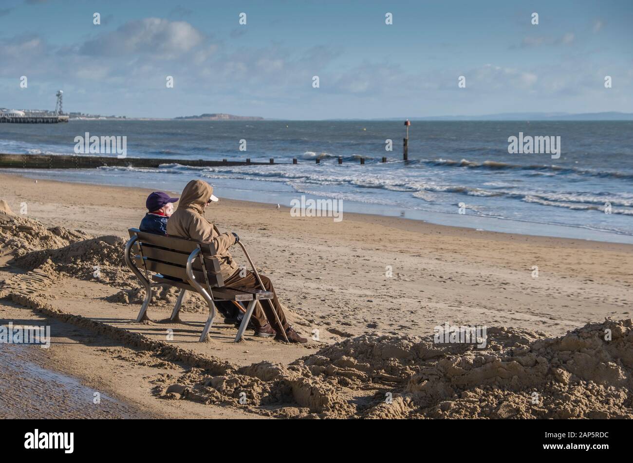 Bournemouth Beach with a mature couple sitting alone on the promenade in winter. Stock Photo