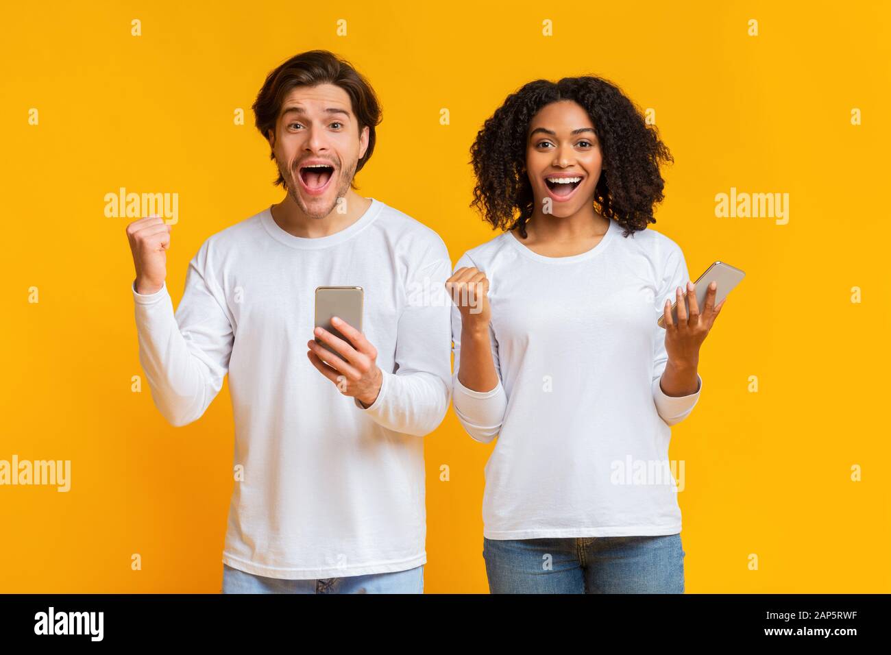Portrait of overjoyed young man and woman rejoicing success with smartphones Stock Photo