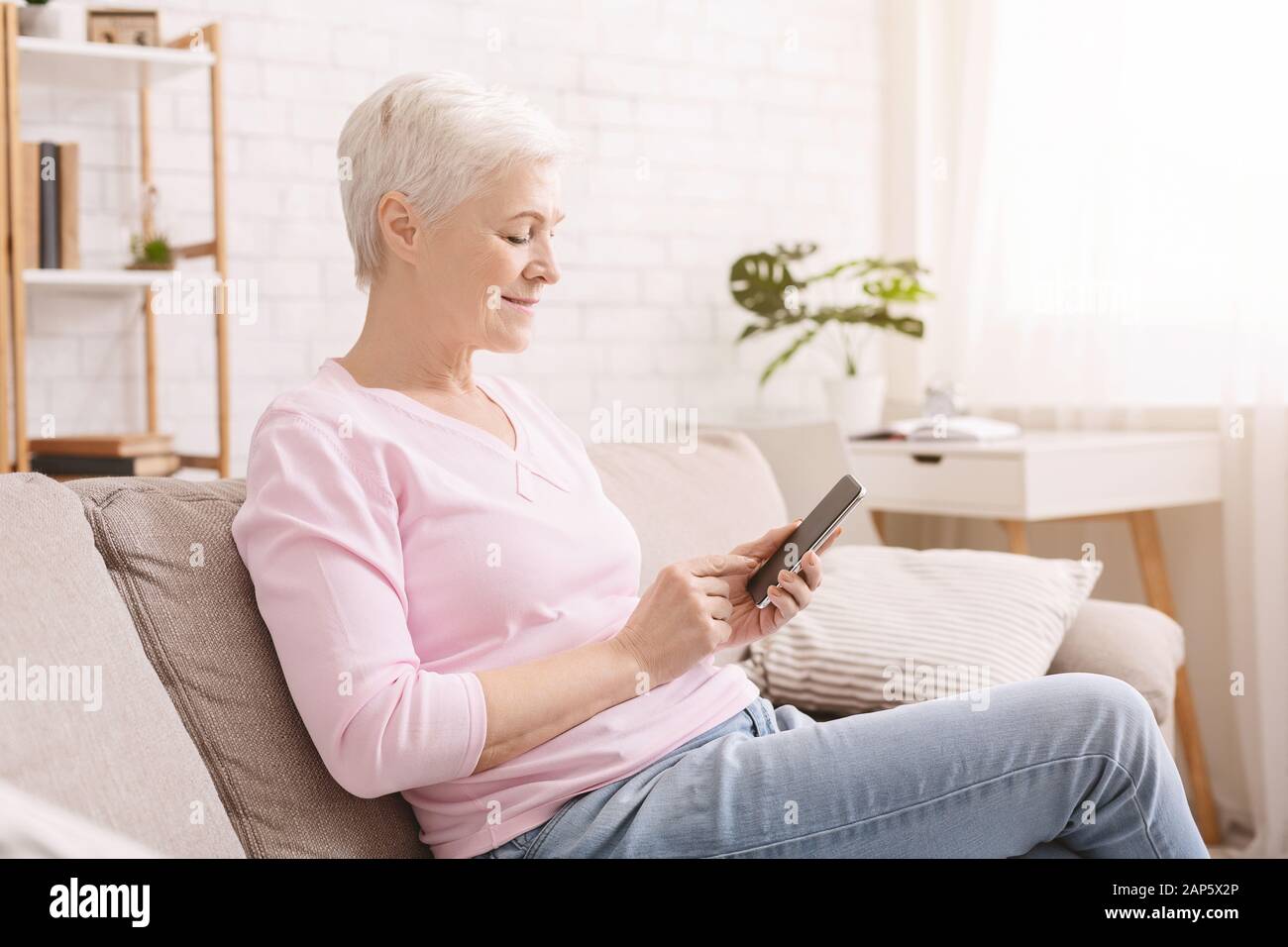 Senior woman chatting on smartphone with friends at home Stock Photo