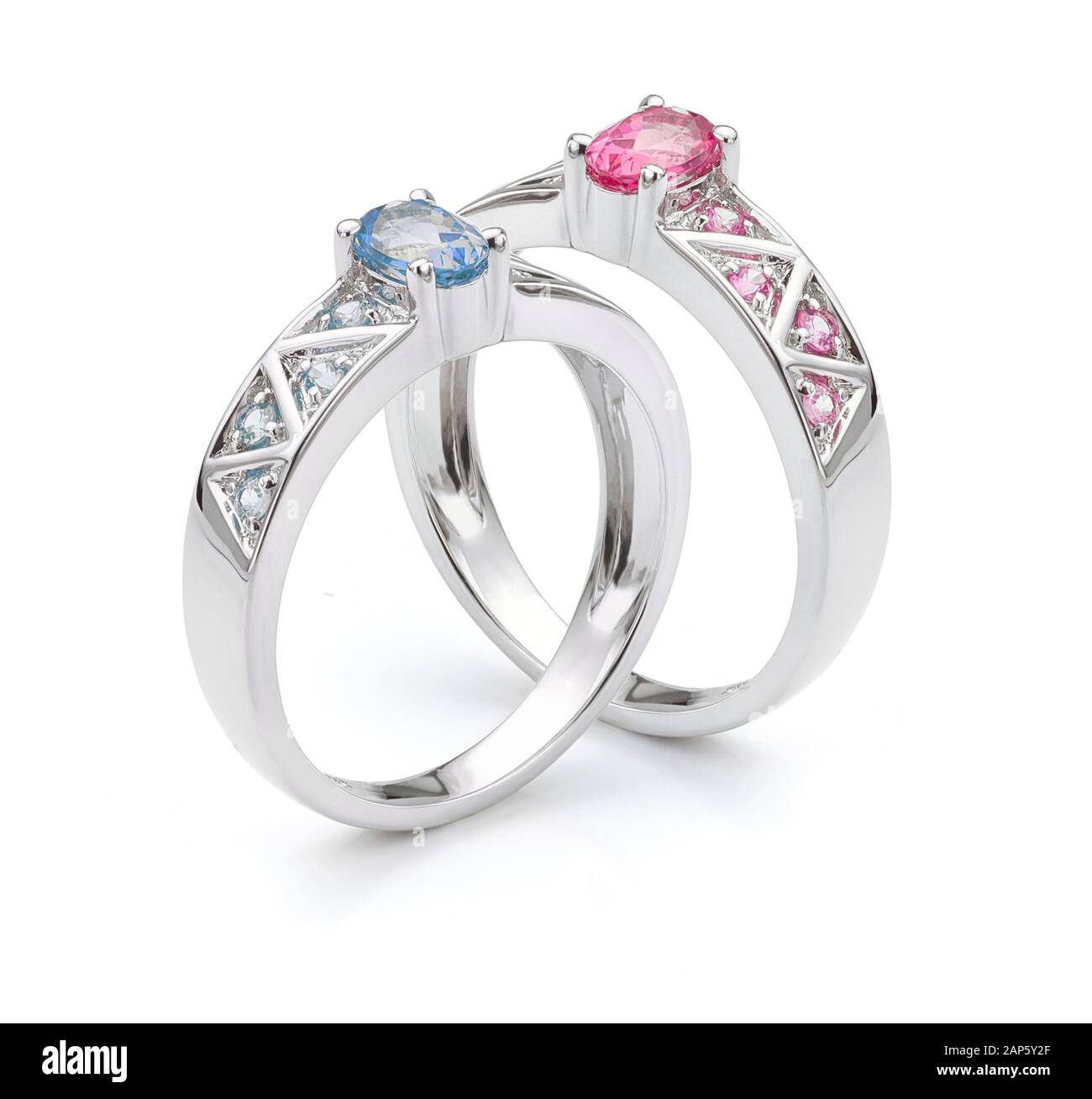 Matching Pink and Blue Sapphire Engagement Rings with Gemstone Shoulders in Silver or White Gold Precious Metal on White Background. Stock Photo