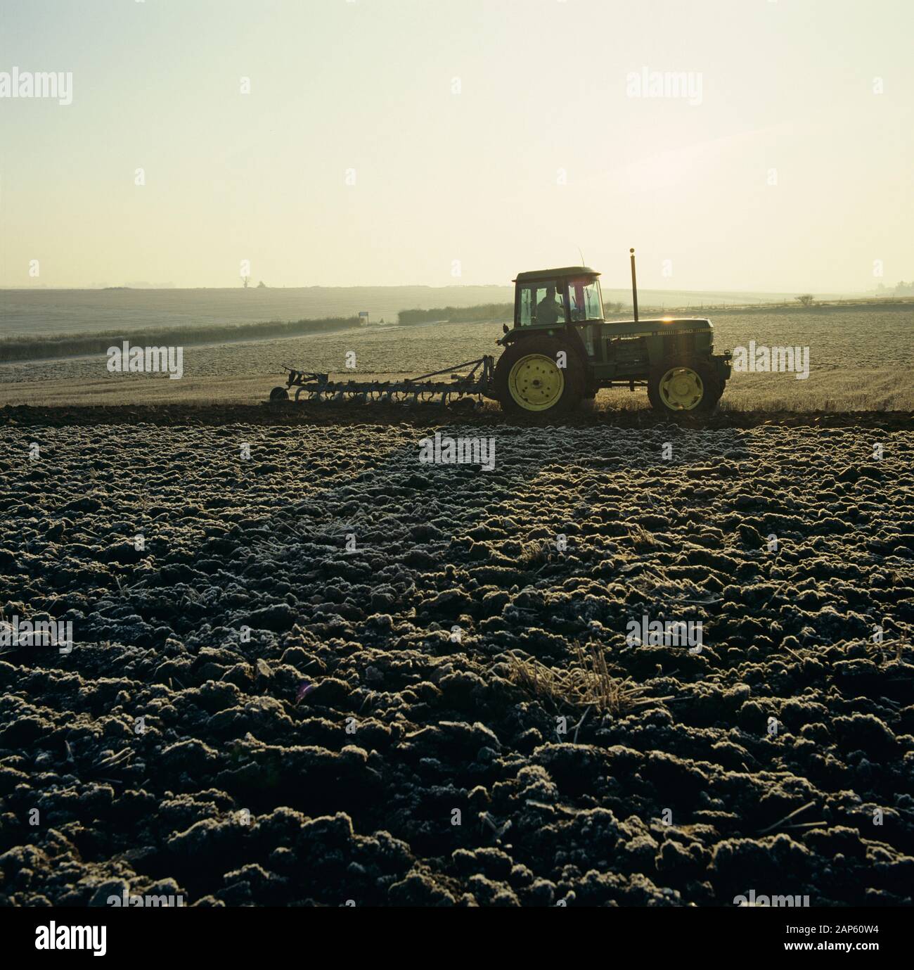 Tractor with a non-reversible, 7 coulter Ransome plough ploughing stubble through the frost on a cold autumn morning, Hampshire, November, Stock Photo
