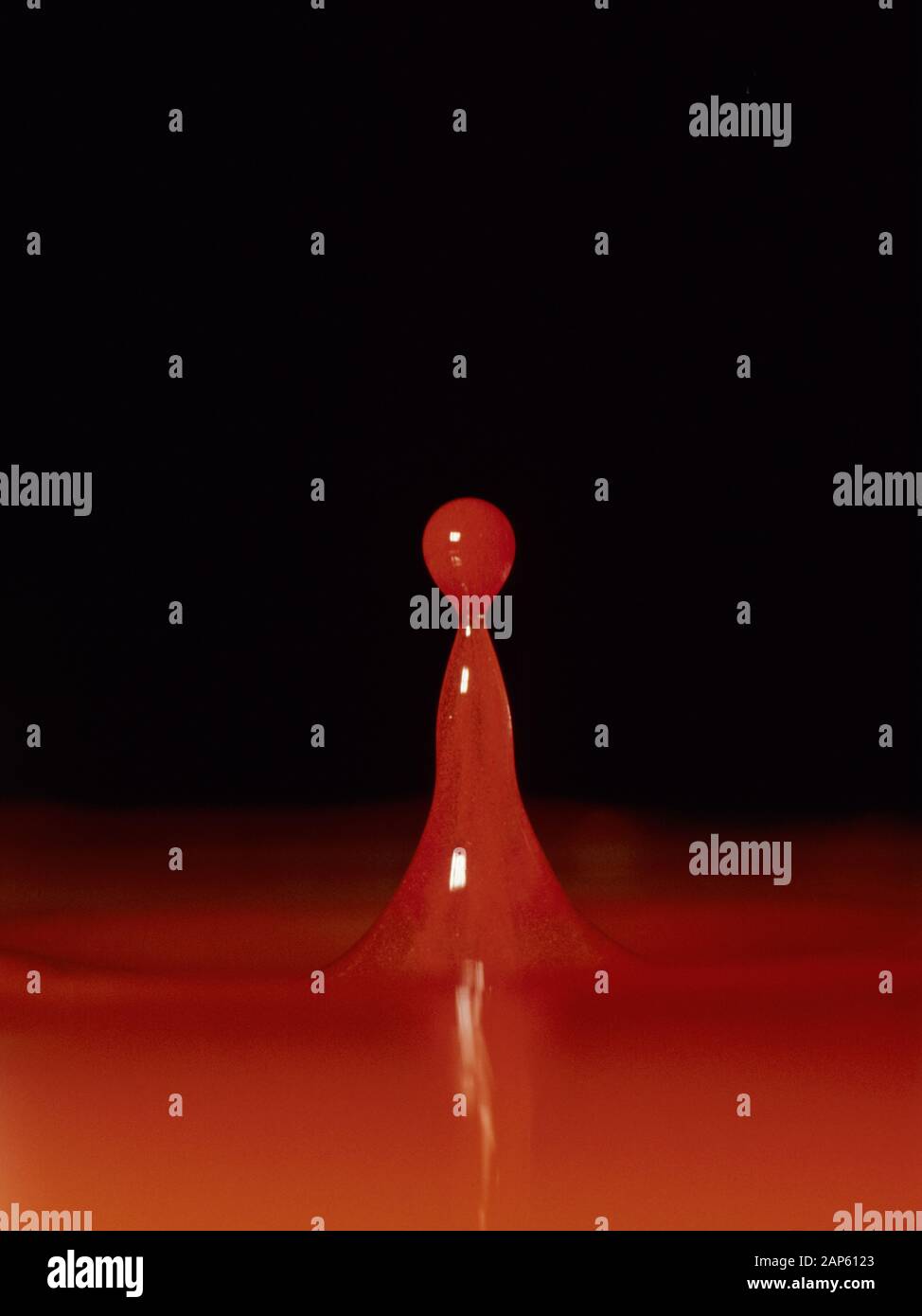 Coluimn of liquid caused by red dyed water droplet falling into shallow water and forming a neck and a satellite droplet as it fass back Stock Photo