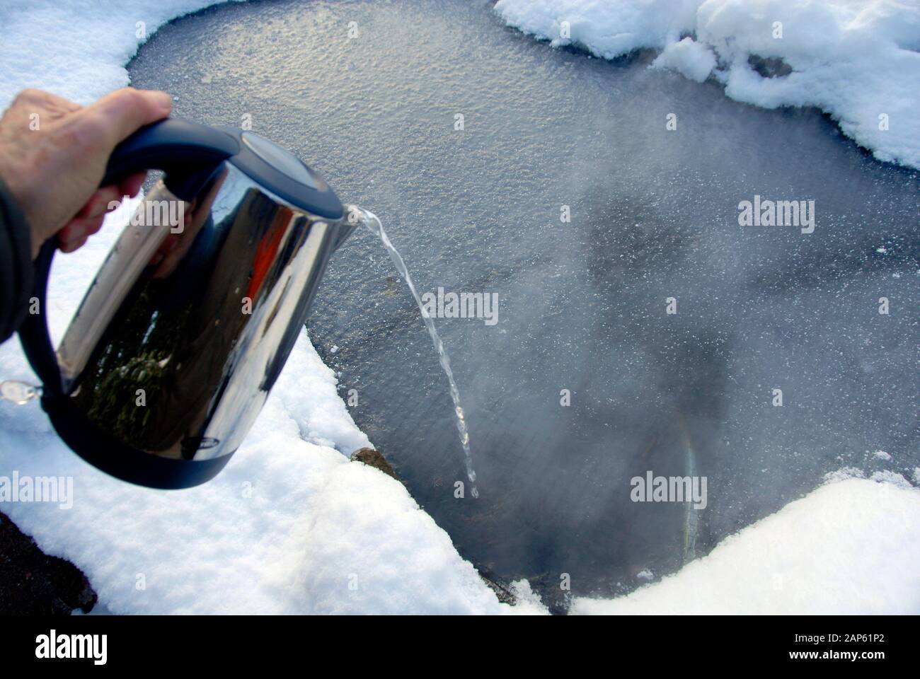 Pouring very hot water from an elecric kettle to melt ice formed on  domestic garden pond Stock Photo - Alamy