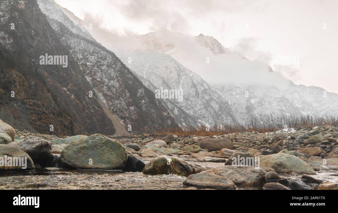 A clear river with rocks leads to the mountains, illuminated by the dawn Stock Photo