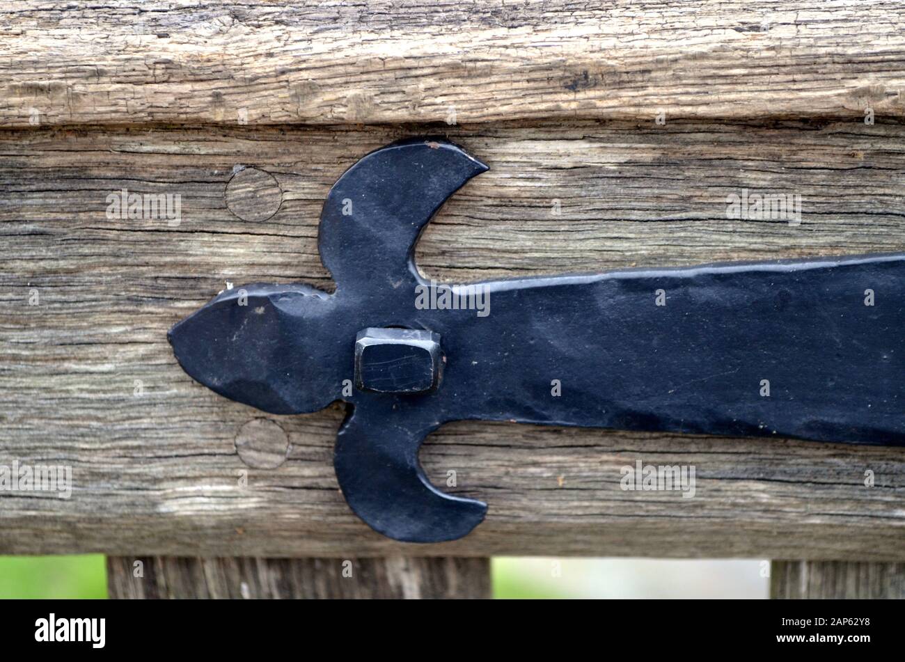 Closeup of a hand-forged barn hinge holding up a wooden garden gate. Stock Photo