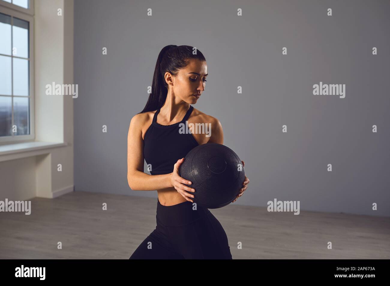 The girl goes in for sports with a medical ball. A sports girl does exercises in a room indoors. Stock Photo