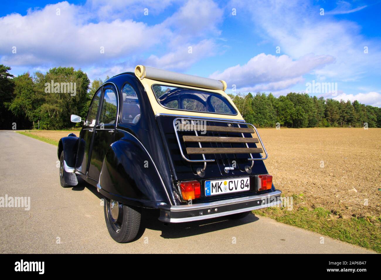 Viersen, Germany - October 12. 2019: Rear view of black French classic cult car 2CV with open roof and wooden luggage rack in rural area against blue Stock Photo