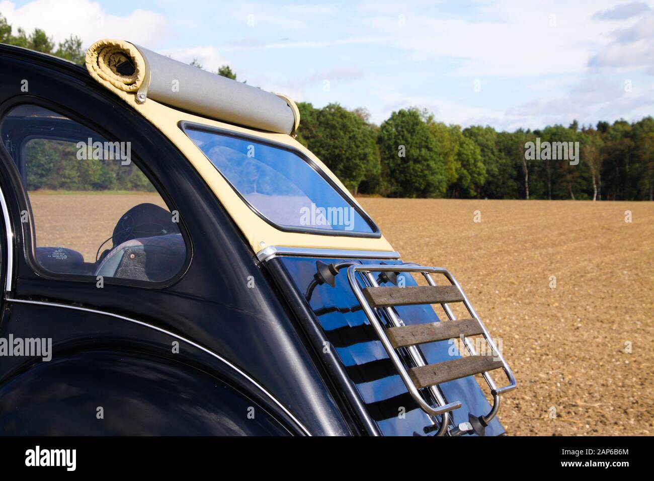 Viersen, Germany - October 12. 2019: Rear view of black French classic cult car 2CV with open roof and wooden luggage rack in rural area against blue Stock Photo