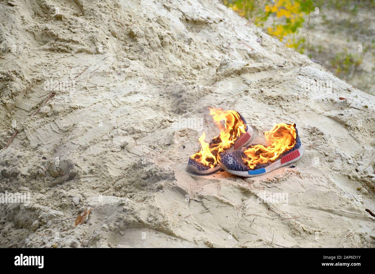 Burning sports sneakers or gym shoes on fire stand on sandy beach coast ...