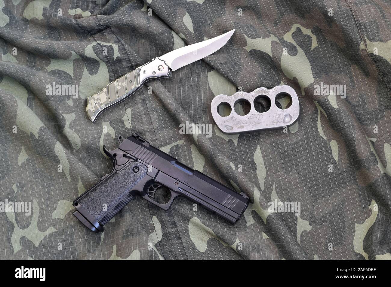 Handgun lies with brass knuckles and knife on camouflage military