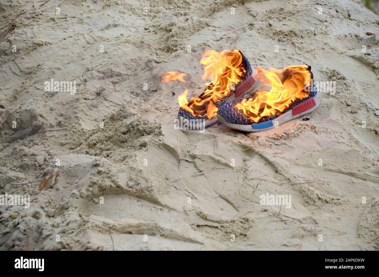 Burning sports sneakers or gym shoes on fire stand on sandy beach coast