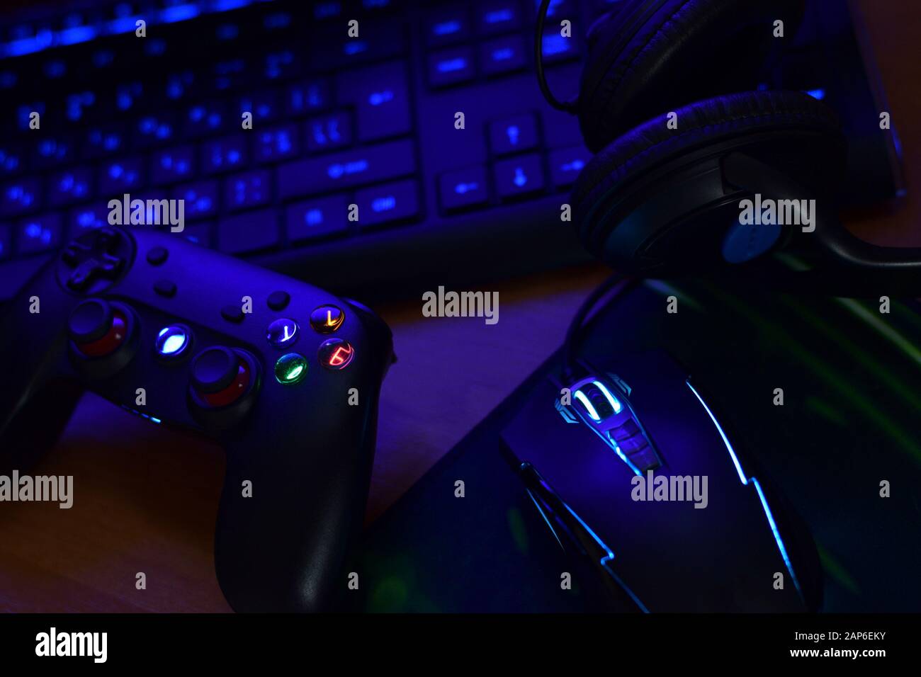 Modern gamepad and gaming mouse lies with keyboard and headphones on table in dark playroom scene close up. Online video game players community concep Stock Photo