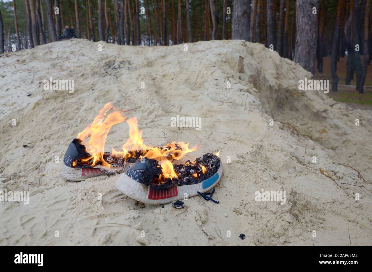 Burning sports sneakers or gym shoes on fire stand on sandy beach coast ...
