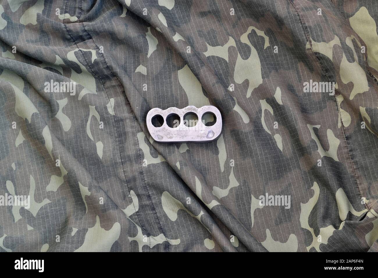 Iron brass cnuckles on crumpled camouflage clothes close up. Football