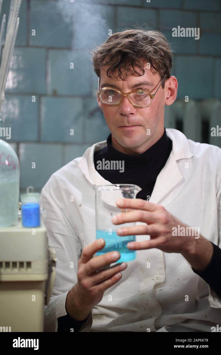 A scientist in a white coat is holding a beaker with a blue reagent