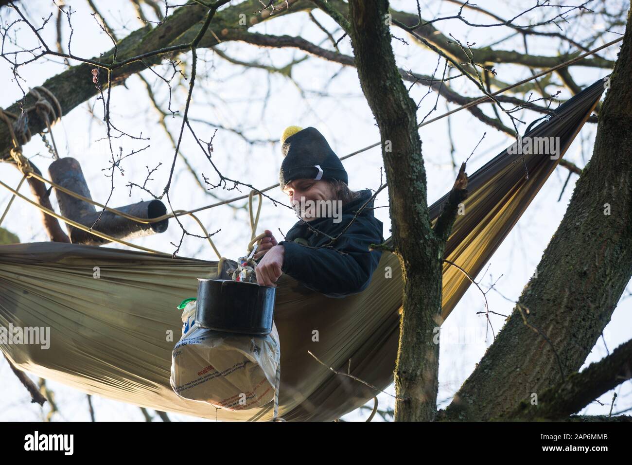 Harefield, UK. 21 January, 2020. An activist lying in a hammock suspended high up in a tree at the Save the Colne Valley wildlife protection camp enjoys a pot of breakfast porridge. Activists seeking to protect ancient woodland threatened by the HS2 high-speed rail link continue to occupy both the roadside and woodland sites of the camp having retaken it from bailiffs acting on behalf of HS2 on 18th January. 108 ancient woodlands are set to be destroyed by HS2. Credit: Mark Kerrison/Alamy Live News Stock Photo