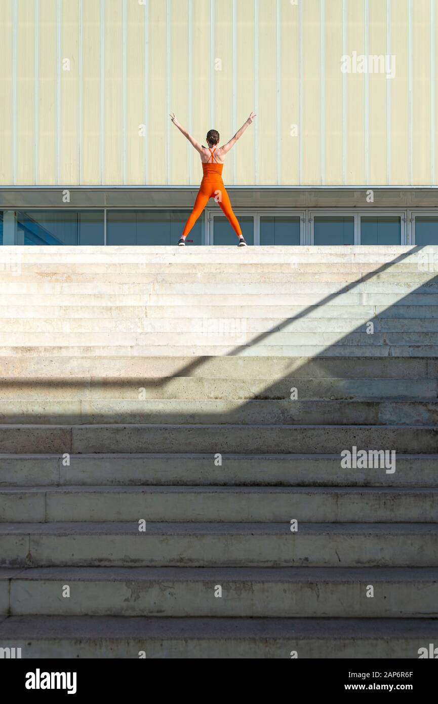 sporty woman at the top of steps with her arms raised, achievement. Stock Photo