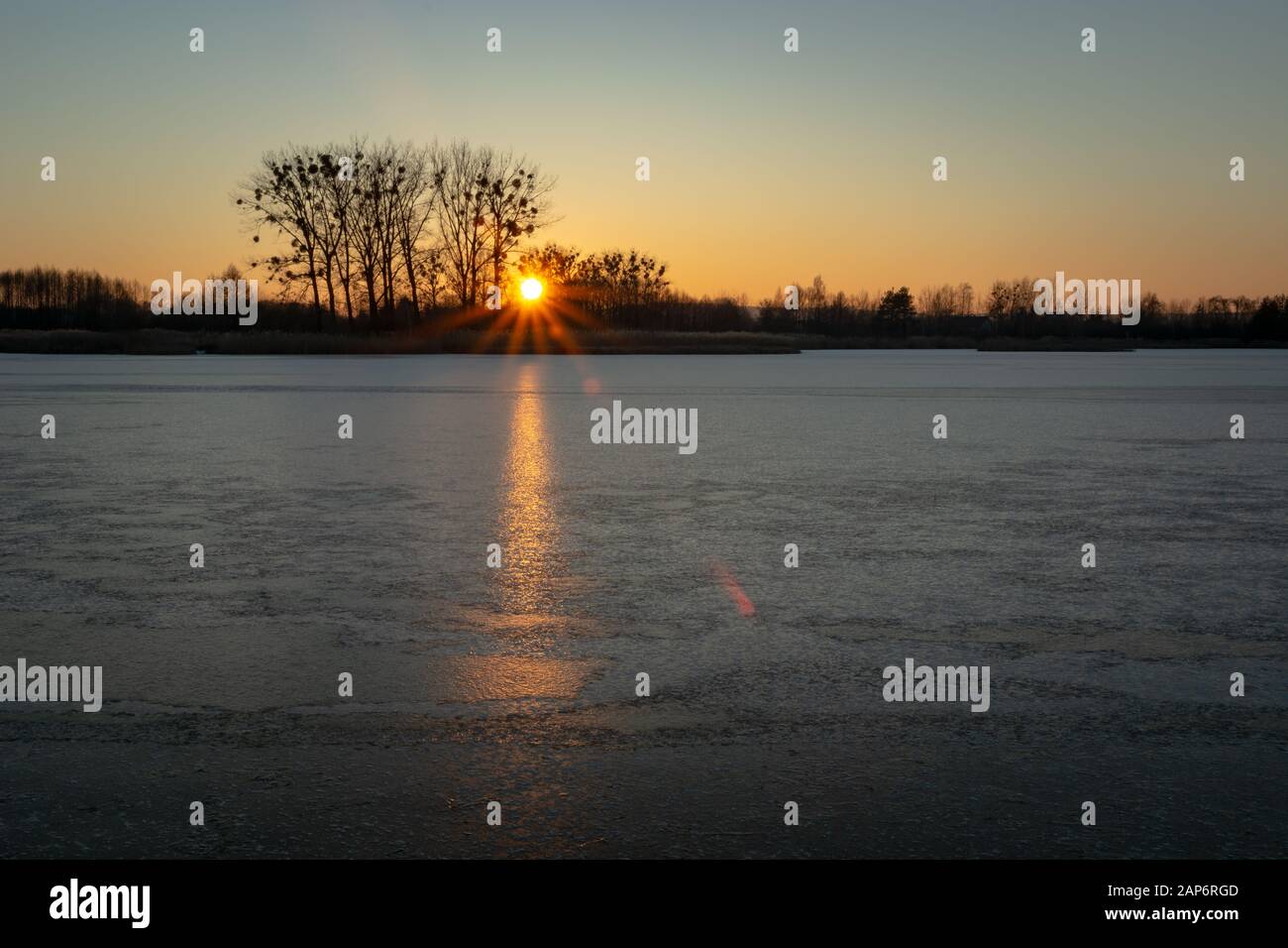 A frozen lake, trees on the horizon and the glow of the setting sun Stock Photo
