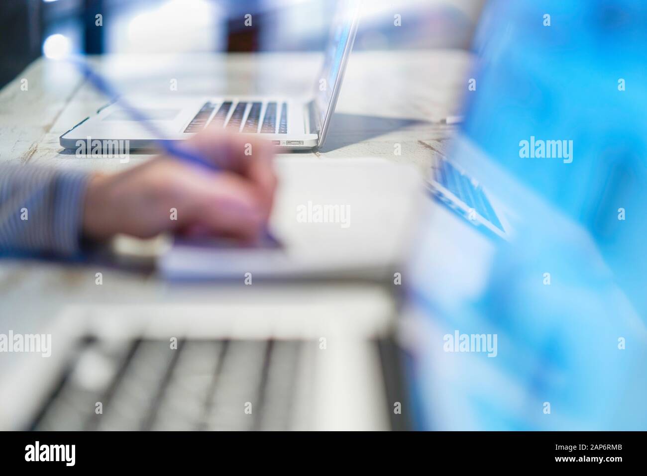 Closeup of hand woman writing working with a pen on a document, close to her computer laptop pc in her home office on her workplace, desktop career sc Stock Photo