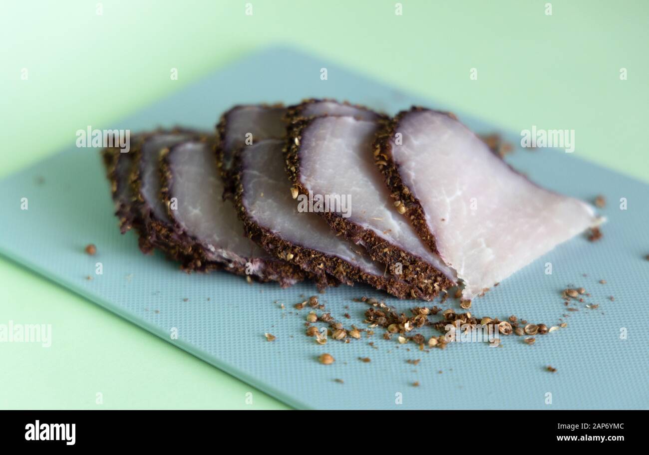 Sliced boiled pork on a blue cutting board on a mint background. An ingredient for a ketogenic diet. Low carbohydrate, high fat. Stock Photo