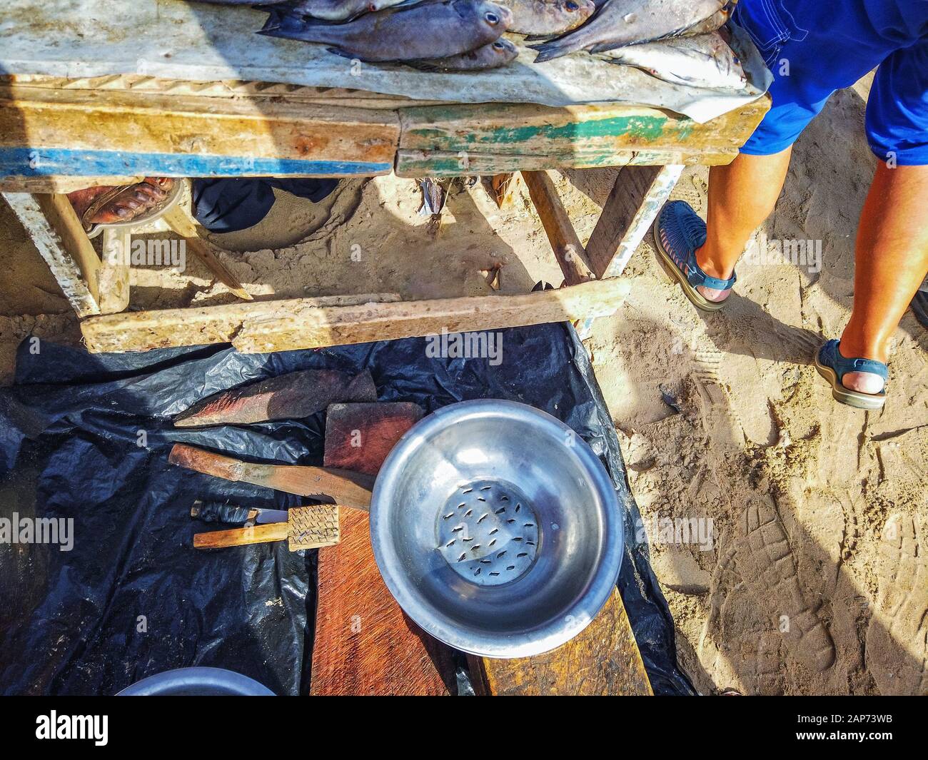 A metal bowl with holes for washing fish lies on a wooden table. It's at the fish market in Mbour, Senegal, Africa. Stock Photo