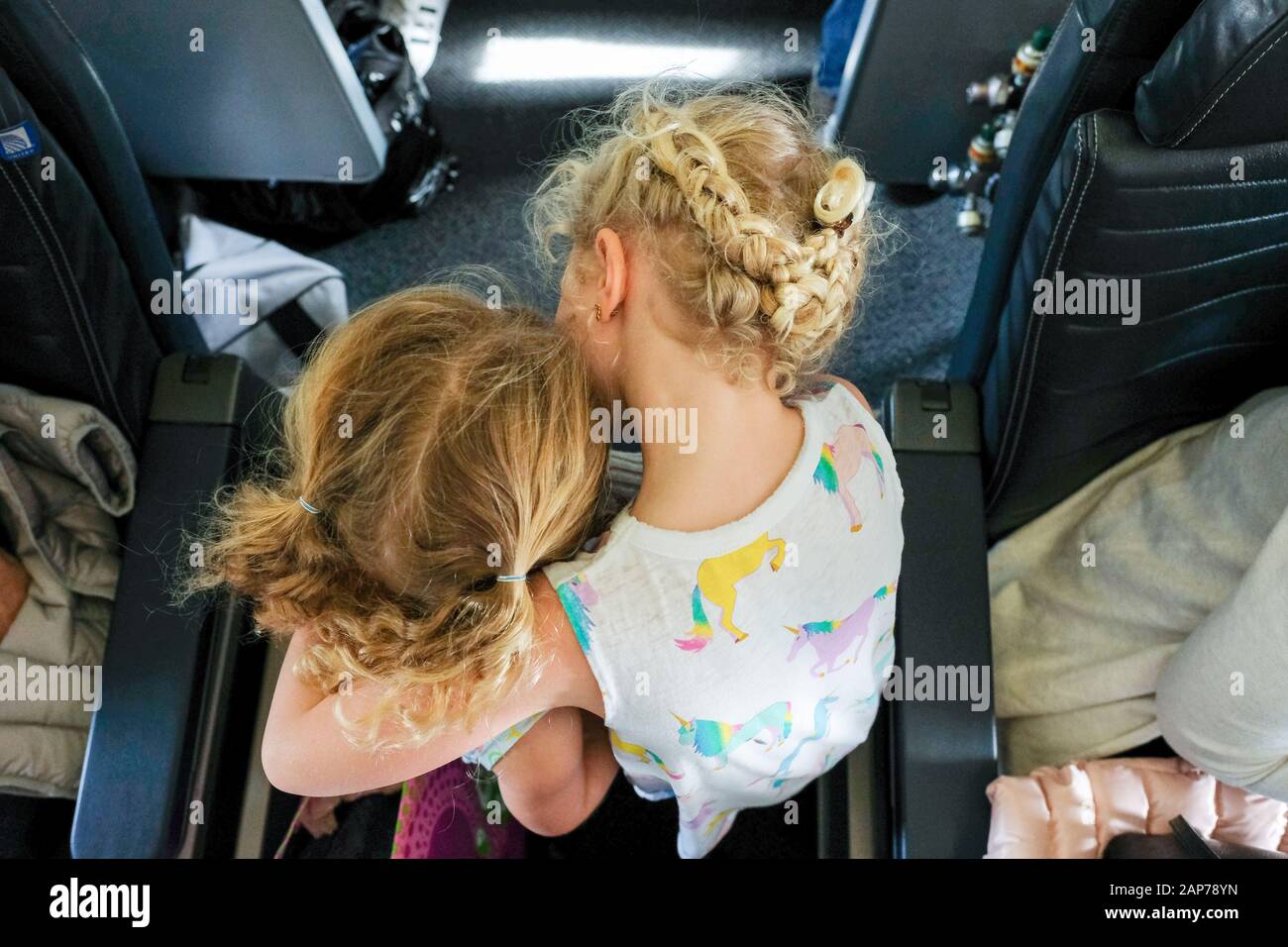sisters walking through airplane aisle towards seat hugging Stock Photo