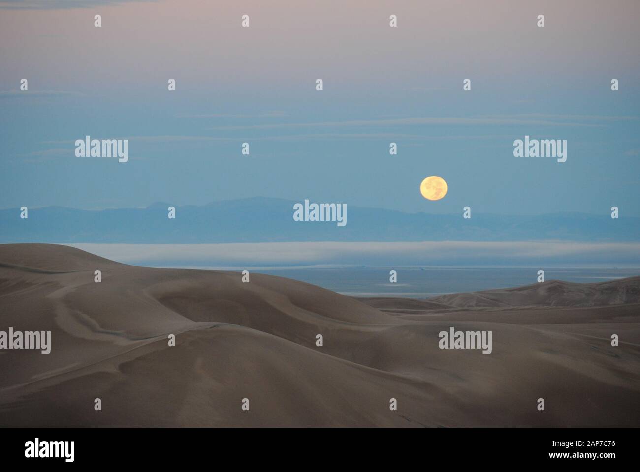 Moon setting over sand dunes Stock Photo