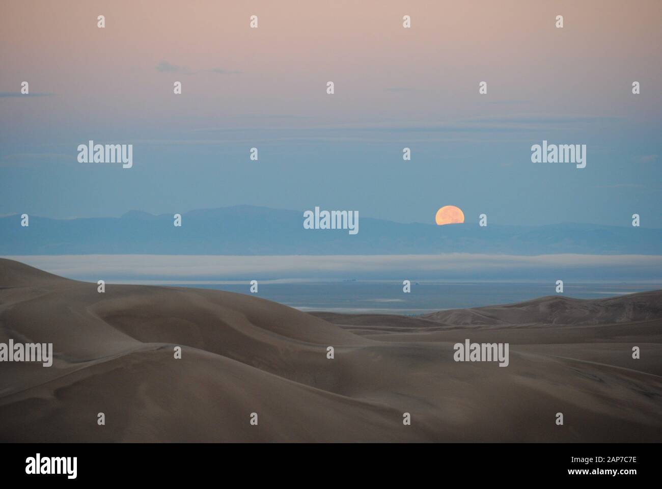 Moon half-setting in sand dunes Stock Photo