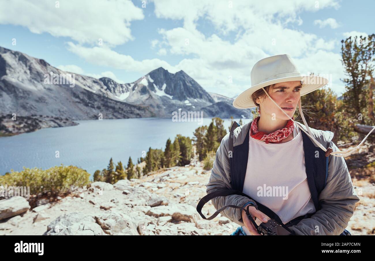 Middle Aged Female in Hat Holding Camera by Lake in Mountains Stock Photo