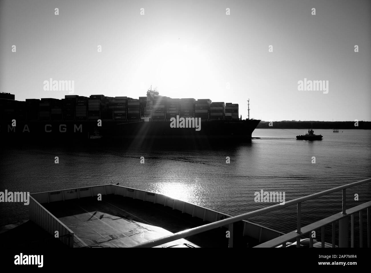 Container ship being guided into port of Southampton by tug late on a January afternoon as the sun prepares to set in the background Stock Photo