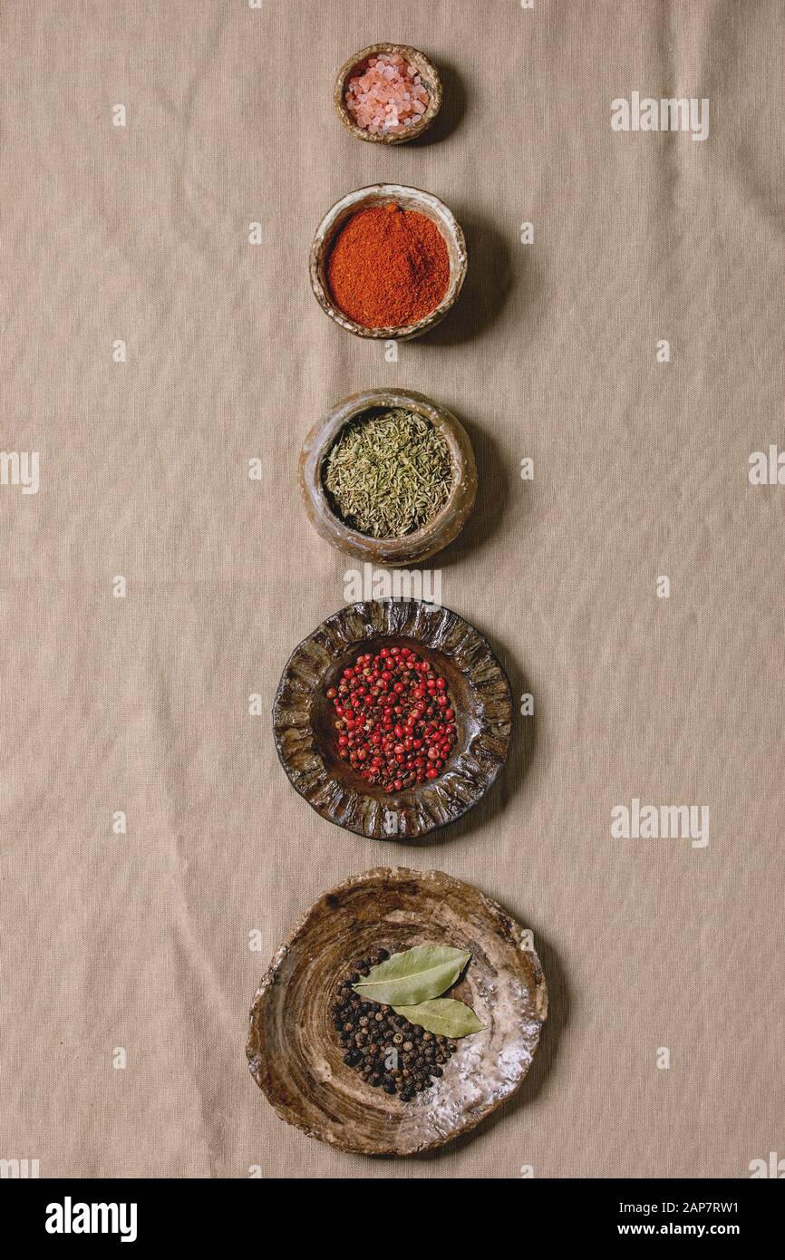 Variety of different handmade ceramic plates and bowls in row with seasonings and spices over grey linen cloth as background. Flat lay, copy space. Ki Stock Photo