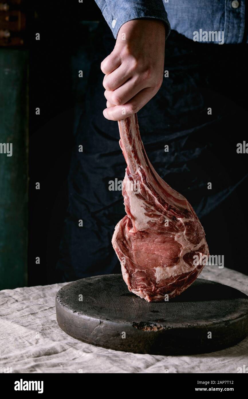 Man's hands holding raw uncooked black angus beef tomahawk steak on bones on linen table cloth. Rustic style Stock Photo