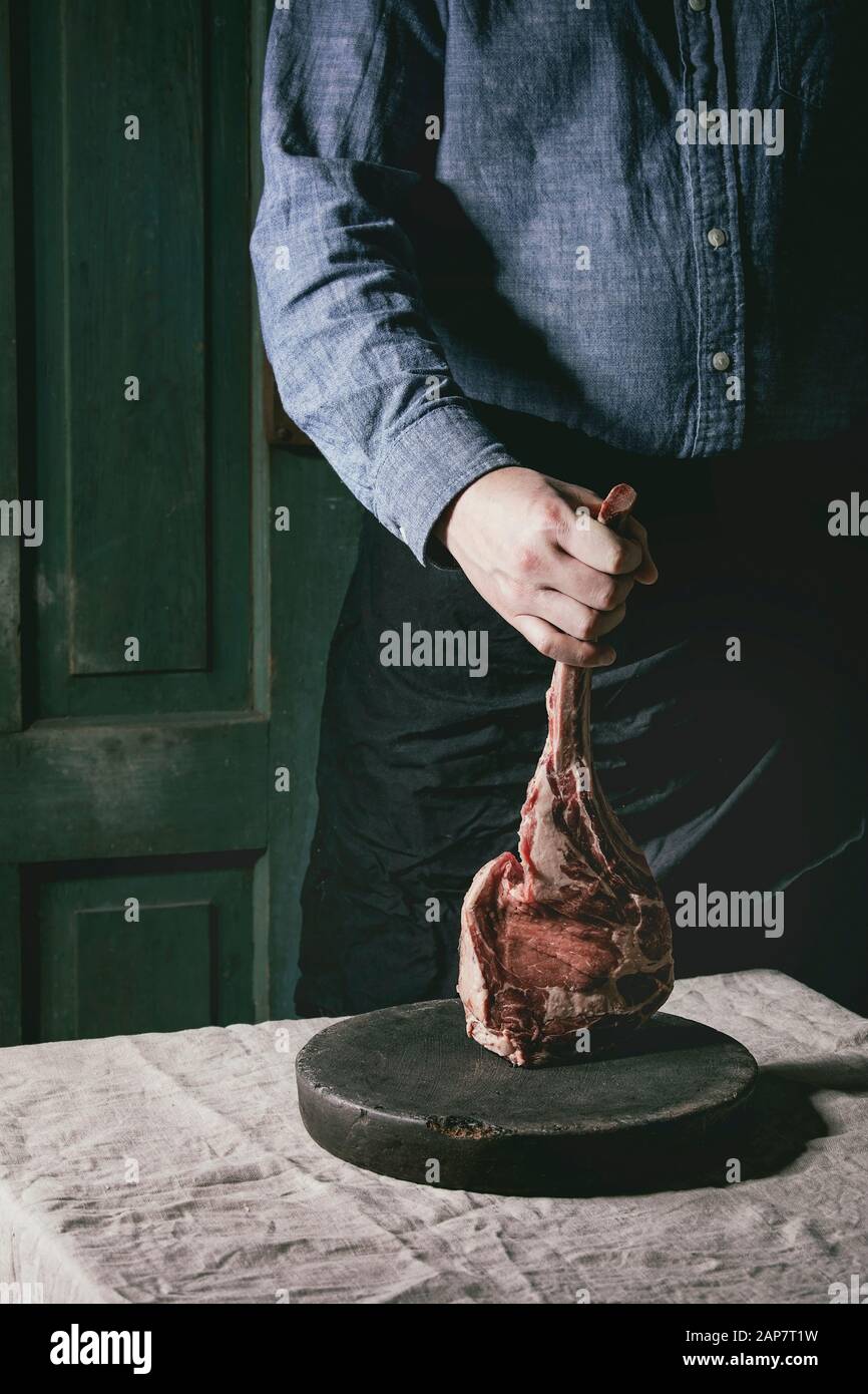 Man's hands holding raw uncooked black angus beef tomahawk steak on bones on linen table cloth. Rustic style Stock Photo