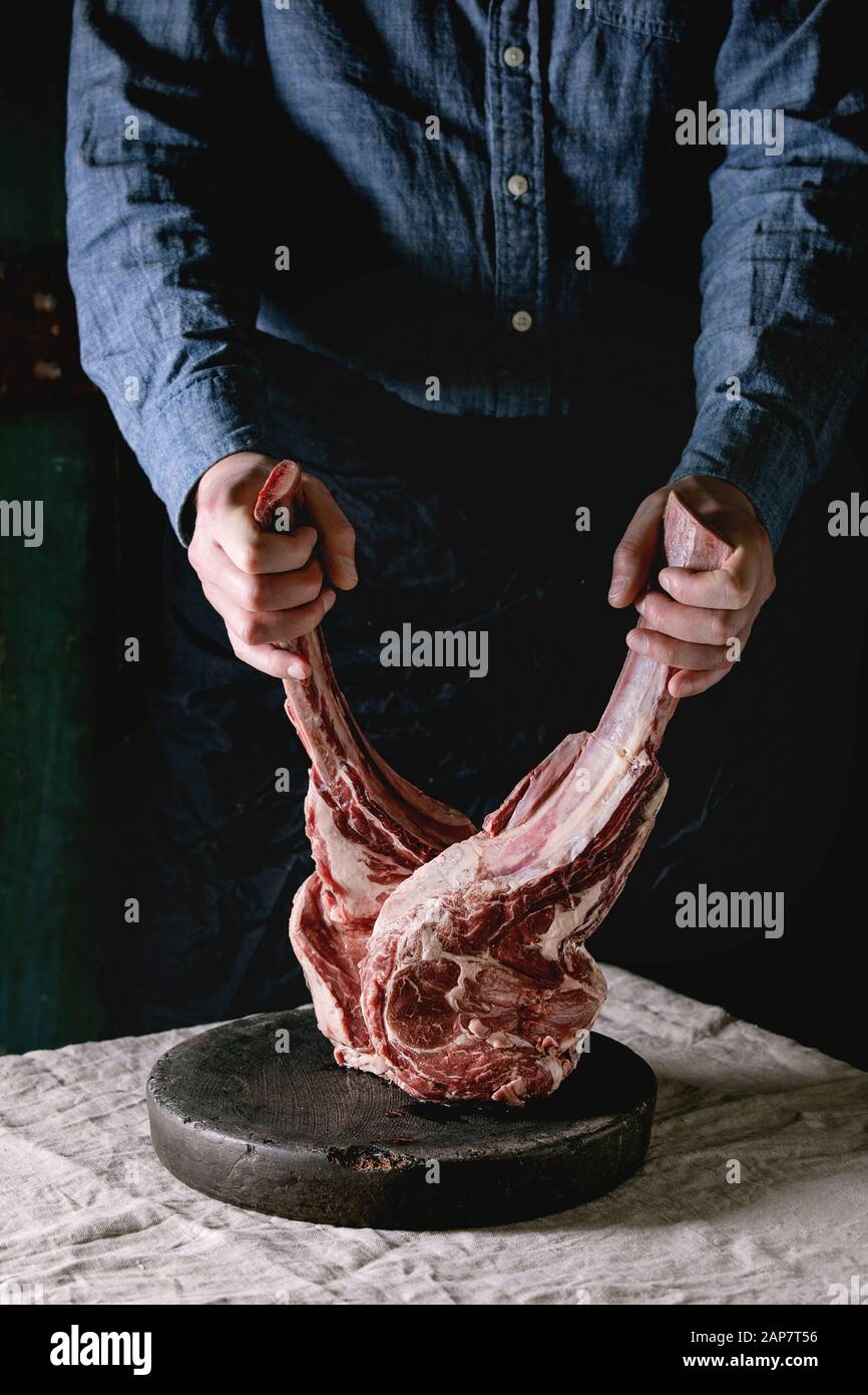 Man's hands holding raw uncooked black angus beef tomahawk steaks on bones on linen table cloth. Rustic style Stock Photo