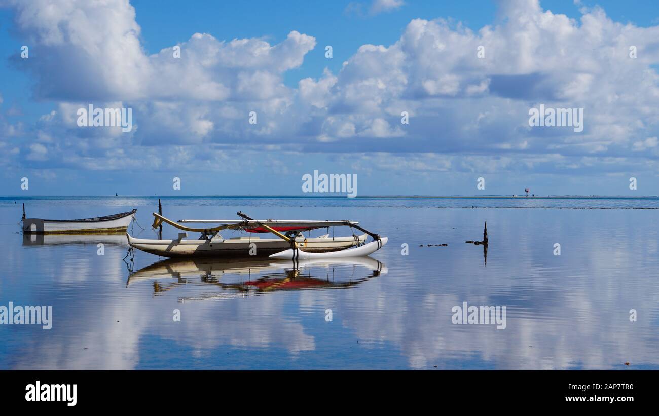 An outrigger canoe sits quietly on the mirror finished waters of Kaneohe Bay in Hawaii Stock Photo