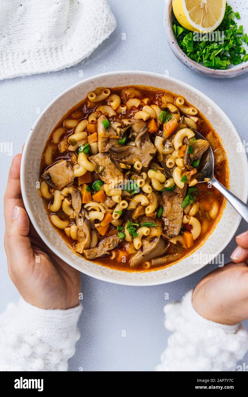 Woman holding a bowl of vegan oyster mushroom soup on a light background Stock Photo