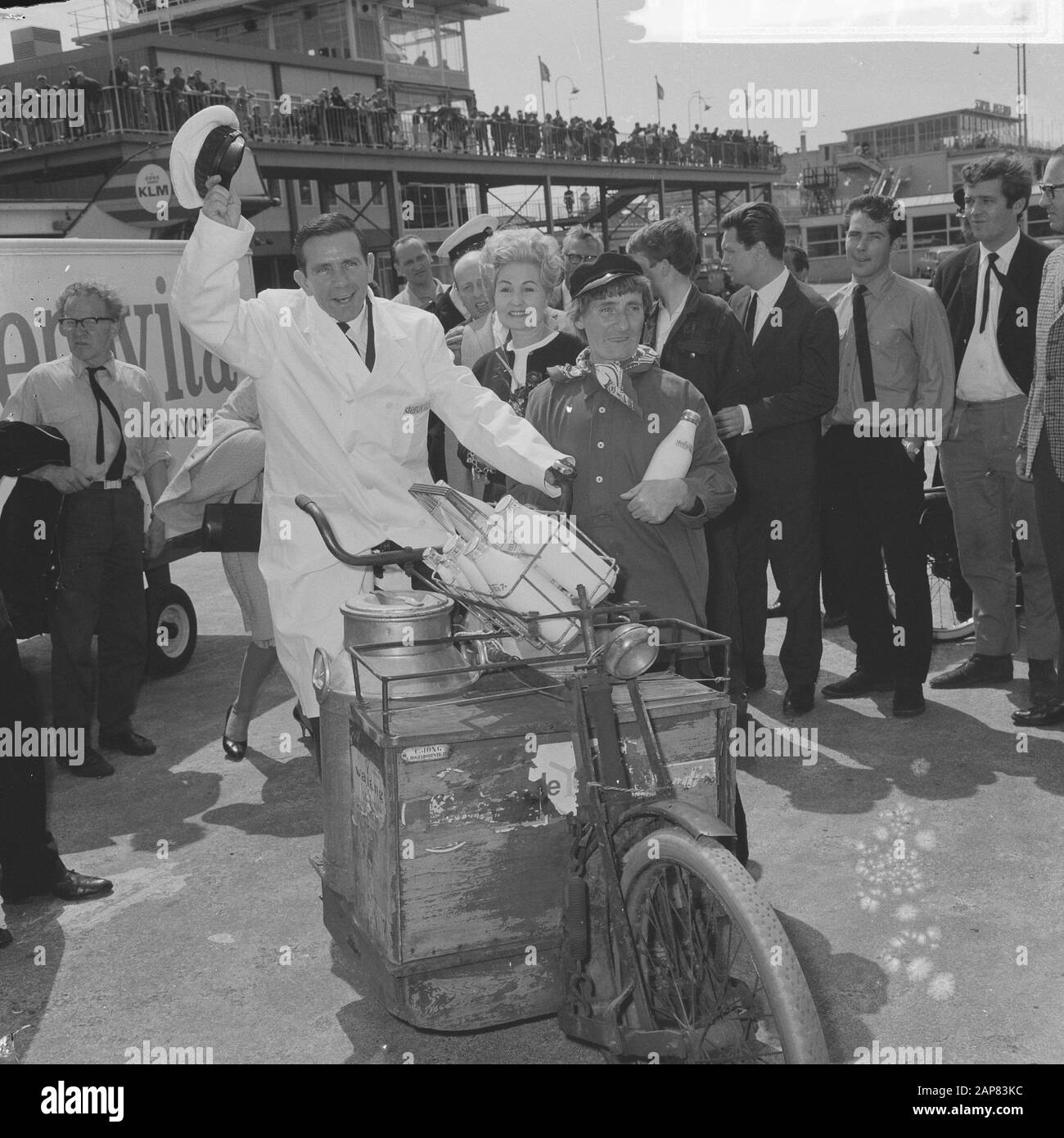 Arrival Norman Wisdom at Schiphol, as a silly milkman he stepped on a transport bike Annotation: Promotion for the film The Early Bird Date: 17 July 1965 Location: Noord-Holland, Schiphol Keywords: actors, movie stars, dairy farmers Personal name: Wisdom, Norman Stock Photo