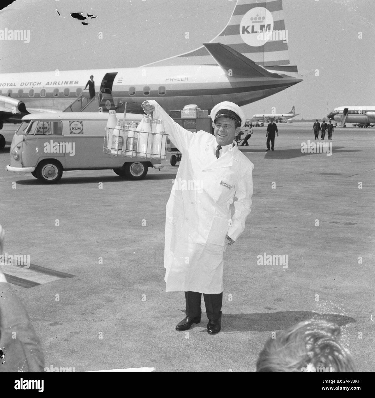 Arrival Norman Wisdom at Schiphol, Norman Wisdom (milk bottle holder in hand) Annotation: Promotion for the film The Early Bird Date: 17 July 1965 Location: Noord-Holland, Schiphol Keywords: actors, movie stars, dairy farmers Personal name: Wisdom, Norman Stock Photo